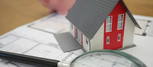 Maqueta de una casa y una lupa sobre unos documentos